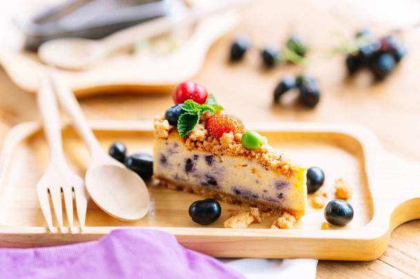 Cheesecake on a wooden plate with a spoon and fork, a popular dessert in a cafe. - Photo, Image