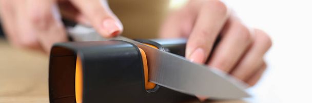 Close-up of woman sharpening knife with special knife sharpener. Grindstone, kitchen tools and devices concept - Photo, Image