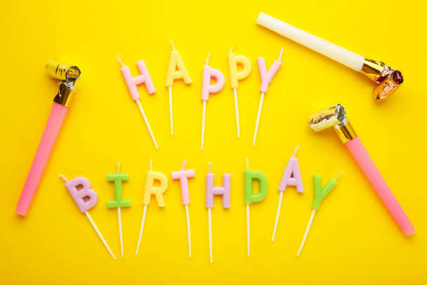 Candele colorate in lettere che dicono Buon Compleanno con il fischio foglio di partito su sfondo giallo. Vista dall'alto - Foto, immagini