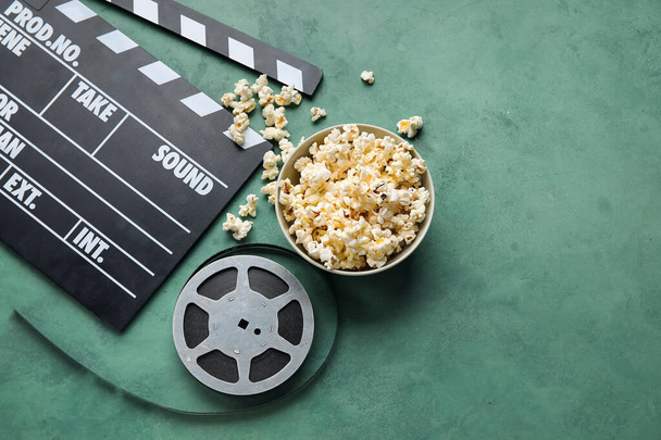 Miska ze smacznym popcornem, klapperem i rolką filmową na zielonym tle - Zdjęcie, obraz