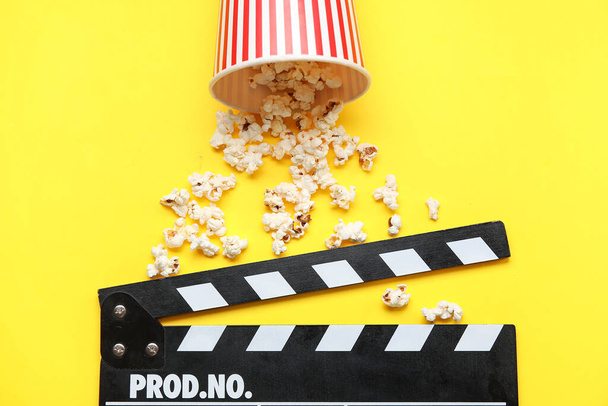 Bucket with tasty popcorn and clapperboard on yellow background - 写真・画像