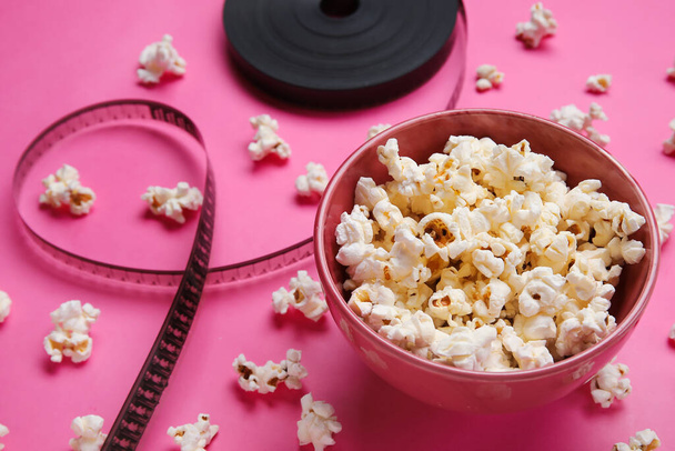 Bowl with tasty popcorn and film reel on pink background - Photo, Image