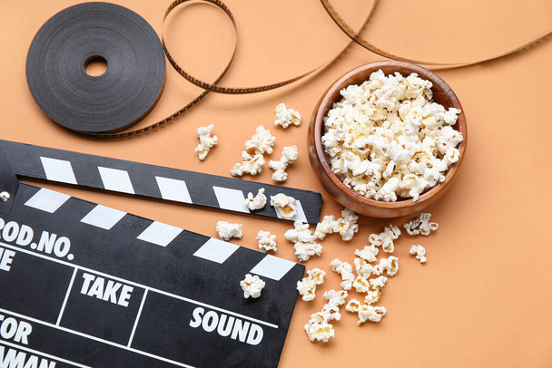 Bowl with tasty popcorn, clapperboard and film reel on brown background - Photo, Image