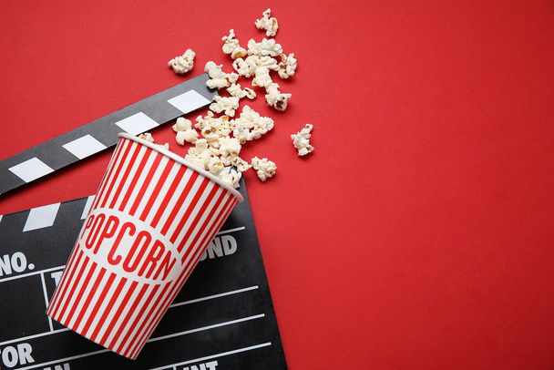 Emmer met lekkere popcorn en clapperboard op rode achtergrond - Foto, afbeelding