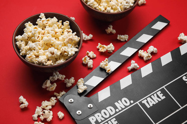 Schalen met lekkere popcorn en clapperboard op rode achtergrond - Foto, afbeelding