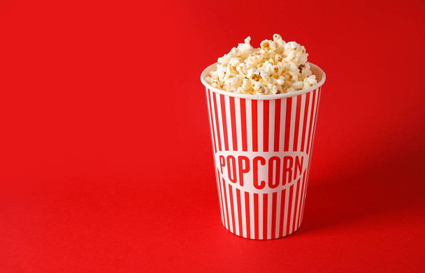 Bucket with tasty popcorn on red background - Foto, afbeelding