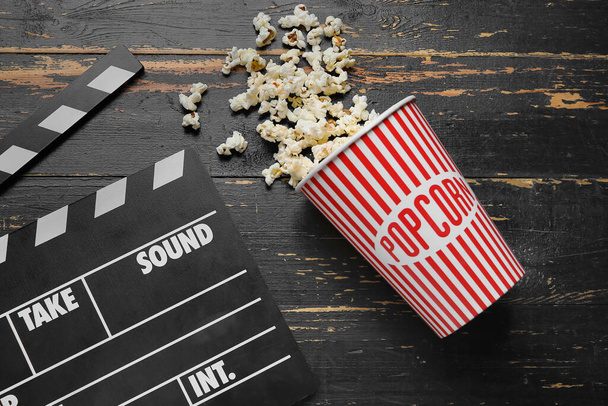 Emmer met lekkere popcorn en clapperboard op zwarte houten ondergrond - Foto, afbeelding