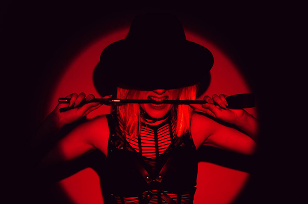 sexy girl in underwear and a hat holds a flogger whip in teeth. BDSM concept of a dominant woman - Φωτογραφία, εικόνα