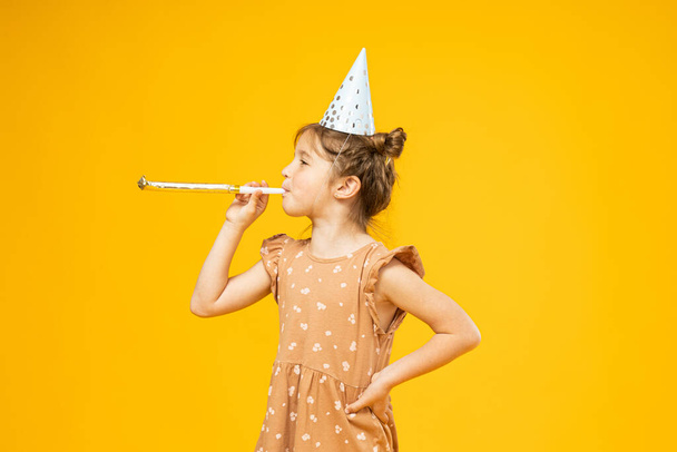 A little girl with a holiday cap on her head on a yellow background - Photo, Image