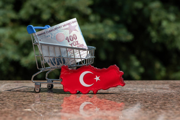 Een symbolische kaart van Turkije, een 100 Turkse lire bankbiljet en een miniatuur winkelwagentje van een supermarkt - Foto, afbeelding