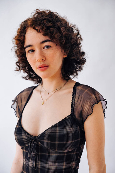 serious woman looking at camera, millennial thinking, curly hair checkered dress - Photo, Image