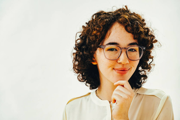 Thinking millennial woman with hand on chin wearing prescription eyeglasses looking at camera - Фото, зображення