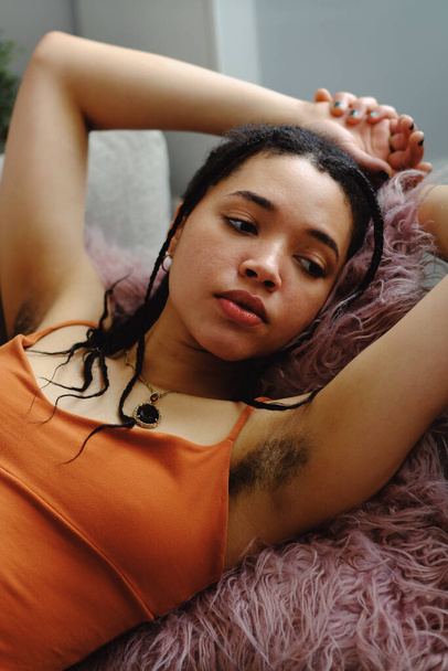 portrait of a young woman with arms raised and armpit hair, natural body, relaxing on sofa - Fotografie, Obrázek