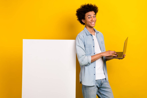 Portrait of positive handsome man use netbook empty space advert blank isolated on yellow color background. - 写真・画像