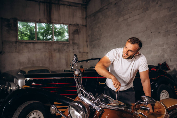 Ein Mann mittleren Alters repariert sein Retro-Motorrad in einer Garage. - Foto, Bild