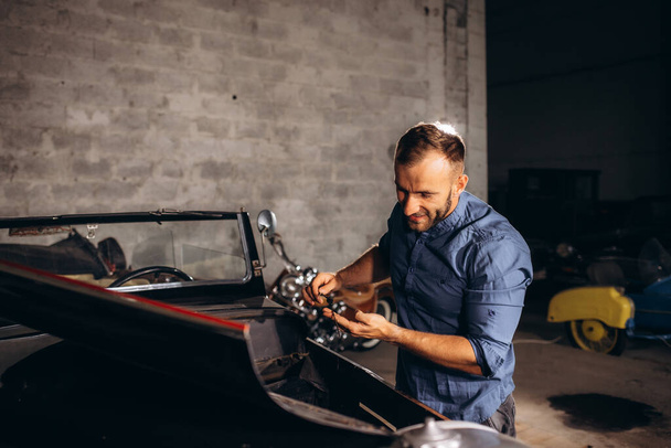 muž středního věku kontroluje hladinu oleje ve svém retro autě v garáži. - Fotografie, Obrázek