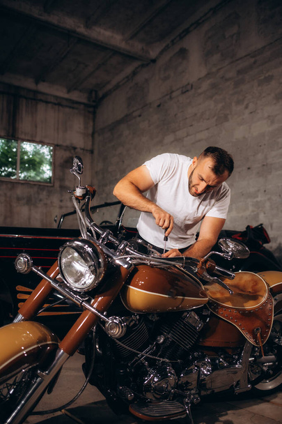 un hombre de mediana edad repara su motocicleta retro en un garaje. - Foto, Imagen