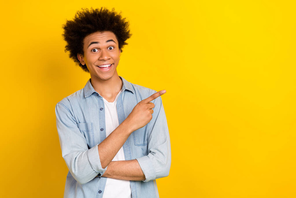 Photo of cheerful excited man wear jeans shirt pointing finger empty space isolated yellow color background. - Fotografie, Obrázek