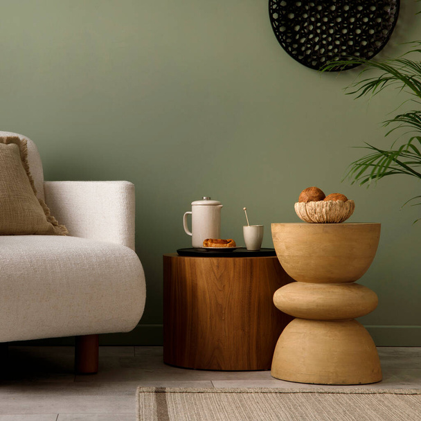 Stylish composition of living room interior with green wall, white armchair with beige pillow. Black ornament on wall. Wooden coffe table with cup, bowl, coconut and vase. Template. - Φωτογραφία, εικόνα