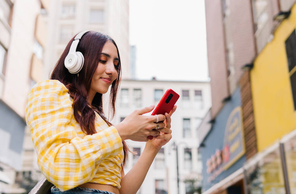 道路のヘッドフォンや携帯電話で音楽を聴いている女性の低角度ビューの写真 - 写真・画像