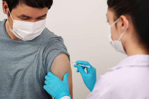 médecin tenant la seringue et faire une injection à l'homme patient dans un masque médical. Vaccin Covid-19 ou coronavirus - Photo, image