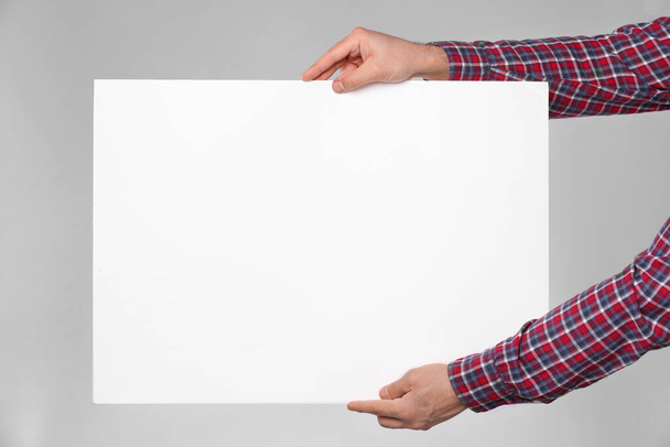 Man holding sheet of paper on grey background, closeup. Mockup for design - Photo, Image