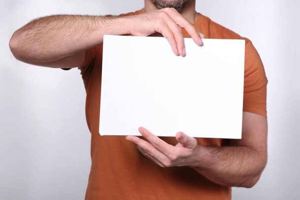 Man holding sheet of paper on light grey background, closeup. Mockup for design - Фото, изображение