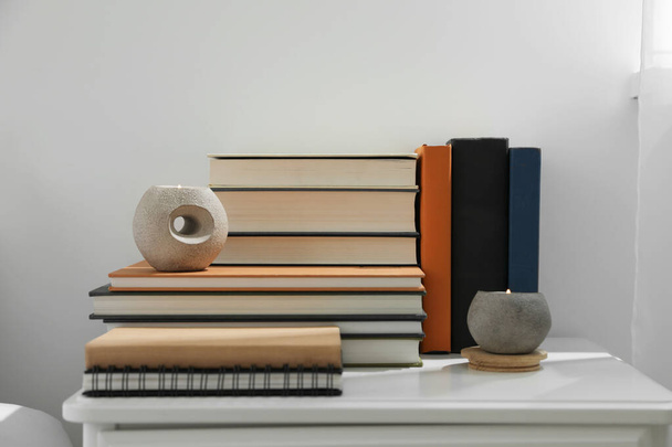 Hardcover books and scented candles on white bedside table indoors - 写真・画像