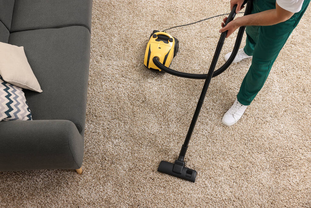 Dry cleaner's employee hoovering carpet with vacuum cleaner indoors, above view - Fotó, kép