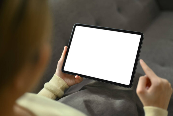 Vista sulla spalla donna seduta sul divano e utilizzando tablet digitale. Schermo vuoto per il tuo messaggio di testo pubblicitario. - Foto, immagini
