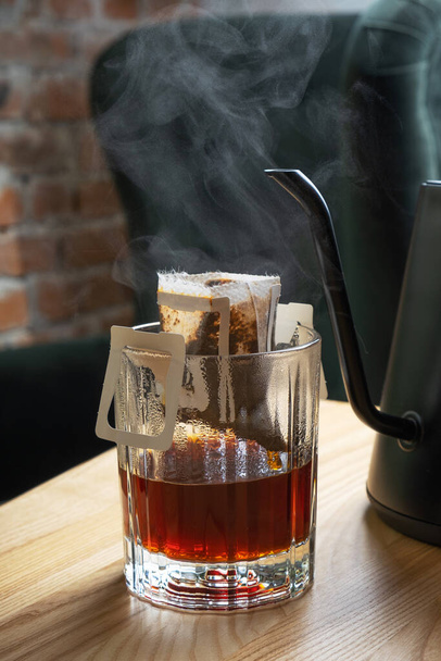 Tropfen Kaffee in einer Glasschale mit einer Teekanne auf einem Holztisch in einem schönen Interieur. - Foto, Bild