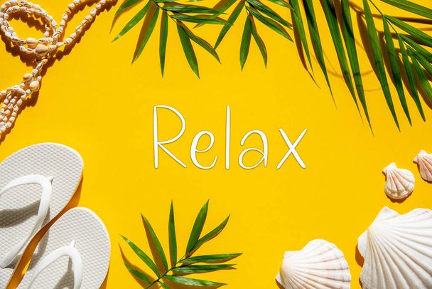 Flat Lay With English Text Relax. Yellow Background With Summer And Maritime Accessories Like Shells, Palm Leafs And Flip-Flops. - Фото, изображение