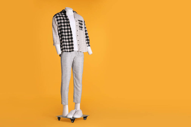 Male mannequin with sneakers dressed in white t-shirt, stylish checkered shirt and pants on orange background. Space for text - 写真・画像