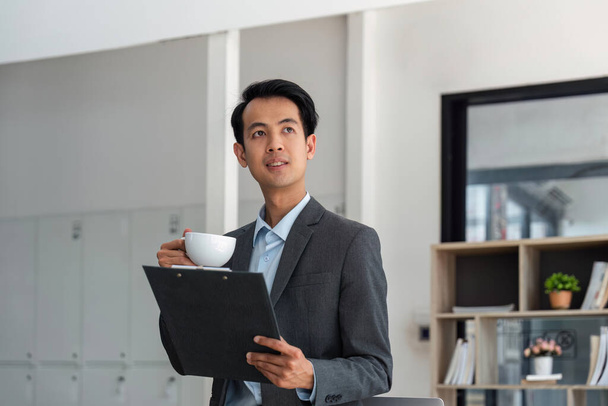 Asie homme d'affaires au bureau et la paperasserie et tenant une tasse de café. - Photo, image
