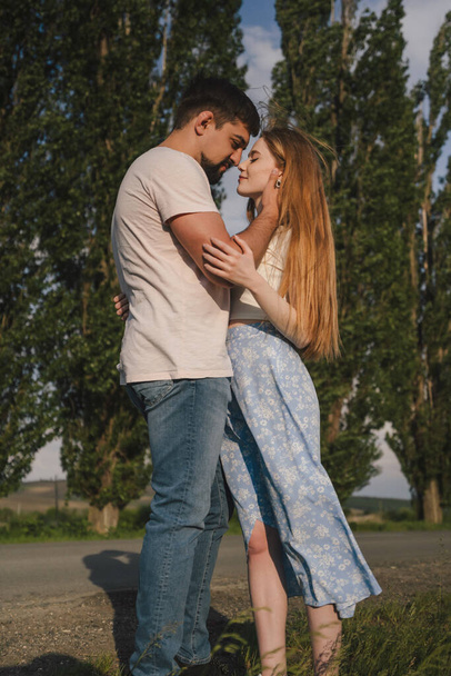 Side view of young couple in casual clothes hugging and kissing each other while standing in green park - Valokuva, kuva