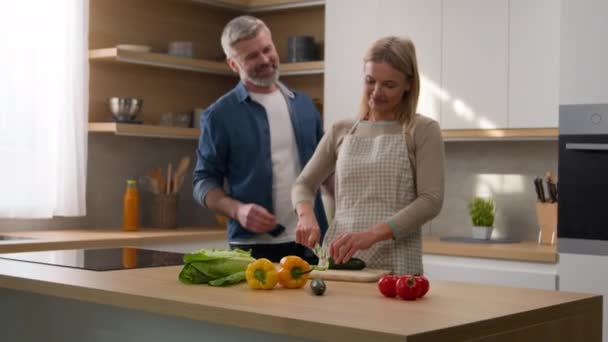 Boldog család kaukázusi középkorú felnőtt a konyhában nő szakács növényi saláta vágott uborka férj férfi ölelés ölelés ölelés ölelés feleség pár beszél diéta élelmiszer szeretetteljes szerelem beszélgetés főzés - Felvétel, videó