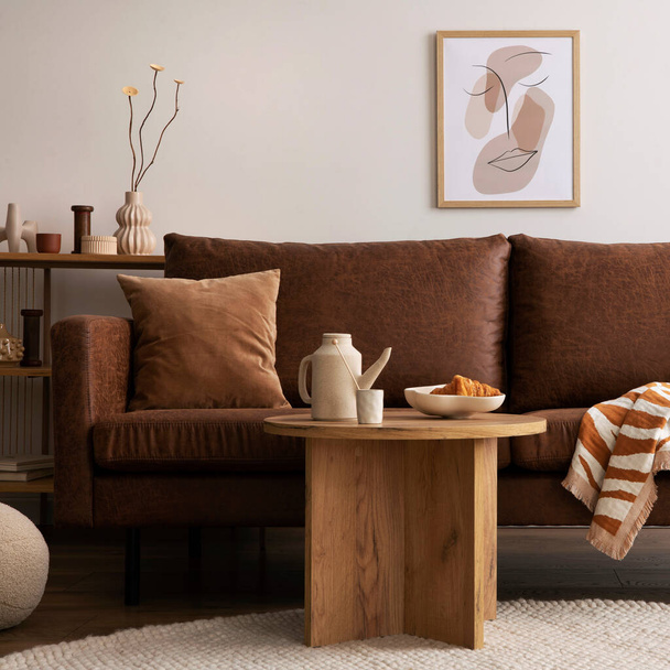 Warm and cozy interior of living room space with brown sofa, round beige carpet, wooden coffee table, mock up poster frames, decoration and elegant personal accessories. Cozy home decor. Template. - Фото, изображение