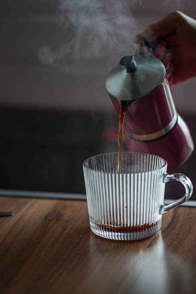 モカ鍋から熱いコーヒーをグラスに注ぐ女。朝のアロマドリンク。おいしい朝食。熱いコーヒーと蒸気 - 写真・画像