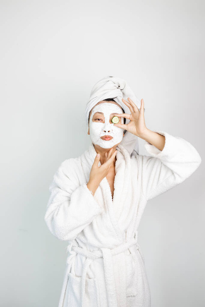 Yüz kilinden maske takan Asyalı bir kız. Güzellik tedavileri. Beyaz arkaplan. - Fotoğraf, Görsel