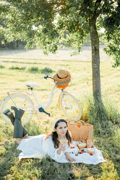 Bella giovane donna dai capelli scuri in picnic sul campo. Modello in abiti alla moda con bicicletta. - Foto, immagini
