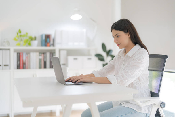 Jovem mulher usando o computador enquanto se senta na cadeira no escritório. - Foto, Imagem
