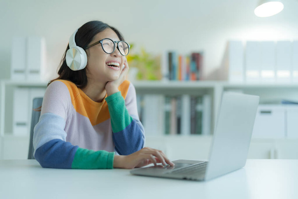 Młoda kobieta lub student korzystający z laptopa w bibliotece w okularach i słuchawkach. Uśmiecha się i wygląda na szczęśliwą.. - Zdjęcie, obraz