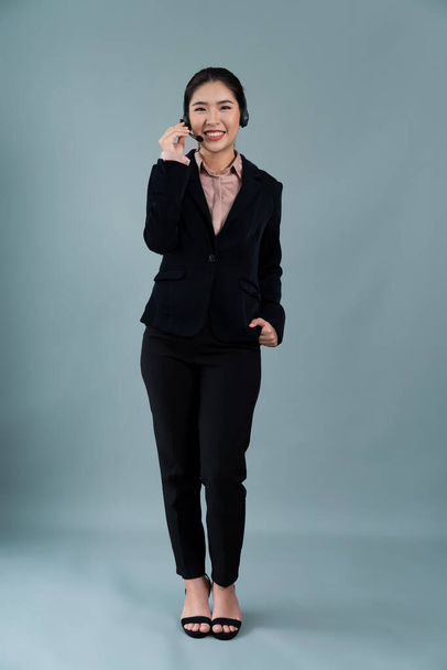 Attractive full body asian female call center operator with happy face advertises job opportunity on empty space, wearing formal suit and headset on customizable isolated background. Enthusiastic - Valokuva, kuva