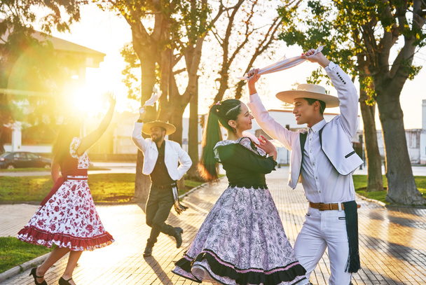 группа из четырех латиноамериканских молодых людей, одетых как танцующая куэка хуасо на городской площади на закате - Фото, изображение