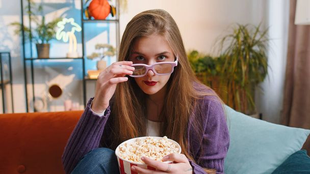 Mujer emocionada en gafas 3D se sienta en el sofá comiendo bocadillos de palomitas de maíz y viendo interesante juego de deportes en serie de televisión, cine, contenido de películas en línea de medios sociales en el apartamento en casa. Chica disfrutando del entretenimiento - Foto, imagen