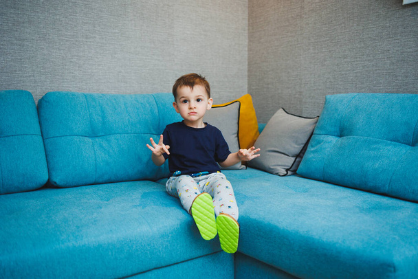 小さな子供の家のエンターテイメントでソファに座っている2歳の男の子. - 写真・画像
