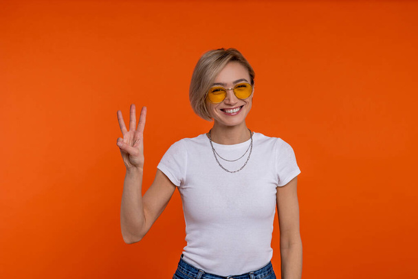Delighted woman in white t shirt showing three fingers isolated over orange background. - Foto, Imagem