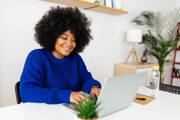 Молода афро-американська жінка, яка користується ноутбуком вдома. Технологія та бізнес концепція. - Фото, зображення