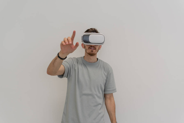 Futuristic man wearing virtual reality glasses interacts with the air in an isolated gray background. High quality photo - Photo, Image