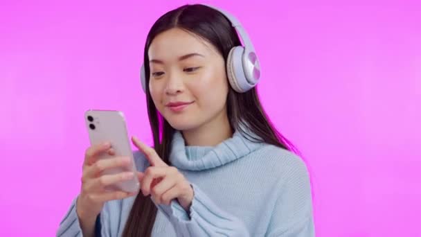 Zene, tánc és telefon egy ázsiai nővel a stúdióban, rózsaszín háttérrel az audió közvetítéshez. Mosoly, szabadság és fejhallgató egy boldog fiatal nő hallgatja a rádió lejátszási lista. - Felvétel, videó